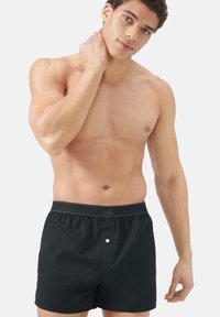 Černé bavlněné boxerky s hladkou texturou, s šedým páskem s logem a jedním předním knoflíkem.