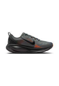 Zapatilla deportiva gris con acentos en negro y naranja, que cuenta con una parte superior texturizada, suela redondeada y un prominente logo Swoosh negro.