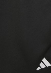 Tejido atlético negro con una sutil textura acanalada y un prominente logo blanco de Adidas en la esquina inferior derecha.