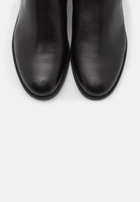 Bottines en cuir noir avec une finition lisse, des orteils ronds et des coutures minimales, dotées d'un profil bas et de semelles robustes.