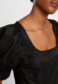 Czarna bluzka z puffowanymi rękawami i kwadratowym dekoltem, z marszczonym materiałem na ramionach i gładką fakturą, odpowiednia na różne okazje.