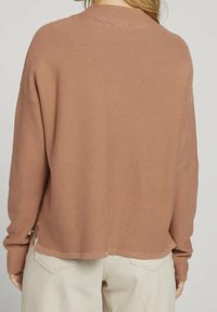 Hellbrauner gestrickter Pullover mit entspannter Passform, überschnittenen Schultern und seitlichen Schlitzen. Die Textur ist weich, mit einem gerippten Halsausschnitt und Saum.