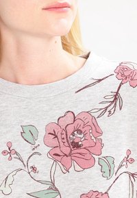 Sudadera gris claro con un diseño floral en tonos rosa y verde, cuello acanalado y textura suave.