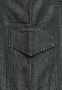 Ciemnoszara tkanina z dużą, kanciastą kieszenią z zarysowanym ściegiem, gładką fakturą i wyglądem przypominającym dżins.