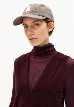Grauer Filzhut mit einem gerundeten Rand und einem weißen gestickten Logo, getragen mit einem tief burgunderfarbenen, gerippten Rollkragenoberteil mit einem V-Ausschnitt.