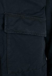 Navy blue fabric jacket with a large patch pocket, visible stitching, and a smooth texture. Features a durable, structured design.