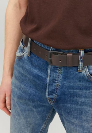 Ceinture en cuir marron avec une finition mate, boucle rectangulaire et cinq trous pour le réglage, portée sur un jean en denim bleu.