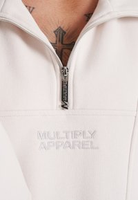 Lys cremefarvet quarter-zip sweatshirt lavet af blødt stof, med et broderet logo og en sølvfarvet lynlås med en mærket trækstrop.