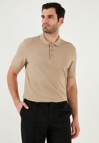 Béžové polokošile s krátkým rukávem a límečkem, se zapínáním na tři knoflíky, vyrobené z texturované látky, v kombinaci s černými kalhotami.