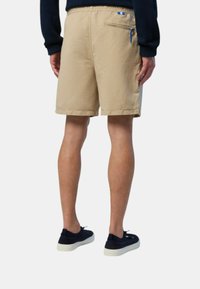 Pantaloni corti beige realizzati in tessuto leggero, con una tasca laterale e un tirante blu. Caratterizzati da una vestibilità rilassata e una finitura semplice all'orlo.