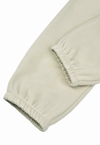 Světle béžové joggingové kalhoty s elastickými manžetami, vyrobené z měkkého bavlněného materiálu. Mají hladkou texturu a jednoduchý, minimalistický design.