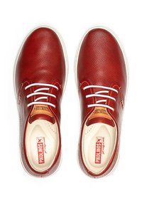 Zapatos de cuero rojo con un acabado texturizado, cordones blancos y una suela en crema a contraste. Presenta un logo en la plantilla. Diseño plano.