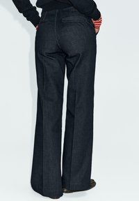 Dark denim wide-leg trousers with a high waist, featuring two back pockets and subtle stitching details.