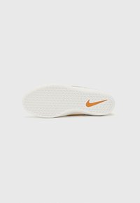 Valkoiset lenkkarit, joissa on kuvioitu pohja, oranssi Nike-logo ja sileä reuna. Pyöreä kärki ja muotoiltu rakenne.