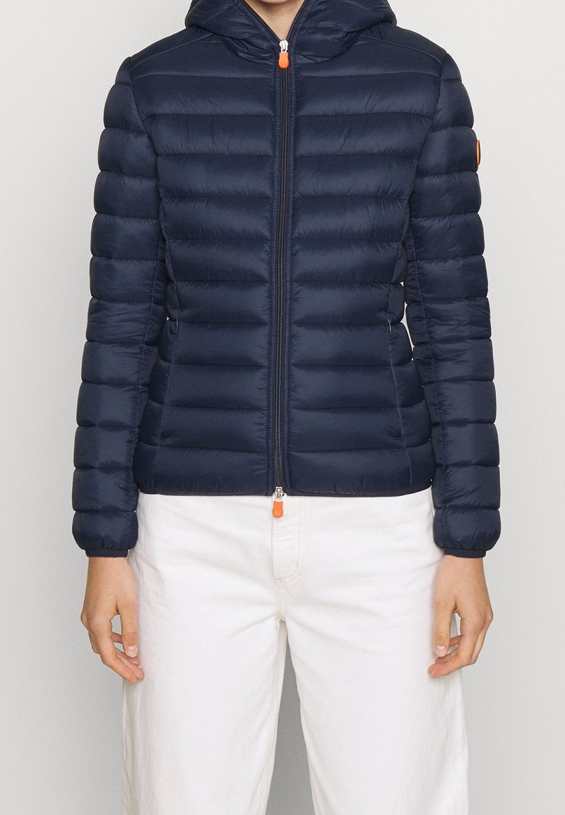 Mørkeblå pufjakke med hætte, der har vandret quiltet design, frontlukning med lynlås og orange lynlåsdetalje. Blød tekstur.