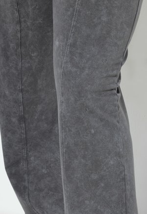 Grijze denim broek met een licht gestructureerd oppervlak, zichtbare naaddetails en een aansluitende pasvorm. De kleur lijkt vervaagd, wat diepte toevoegt.