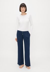 Bílá košile s dlouhým rukávem v kombinaci s námořnickými širokými kalhotami s elastickým pasem a dvěma malými knoflíky ve tvaru srdce.