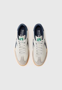 Valged ja tumesinised spordijalatsid, millel on suédest toe cap, nööridega kinnitus ja kummist põhi. Sisetalla peal on roheline Skechers logo.