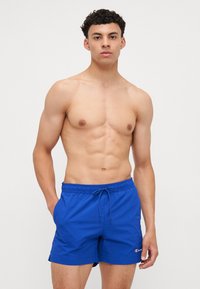 Shorts de bain bleus avec une taille élastique et un cordon de serrage. Fabriqués en tissu léger avec une texture lisse. Accent logo sur la jambe.