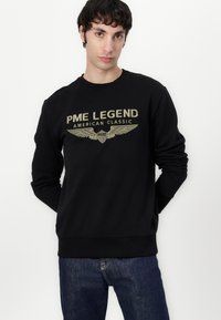 Felpa nera con il testo "PME LEGEND AMERICAN CLASSIC" e grafica di ali in oro, maniche lunghe, collo rotondo e polsini a costine.