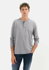 Grå langærmet henley skjorte med tre-knaps placket, afrundet kant og blød tekstur, parret med mørkeblå jeans.