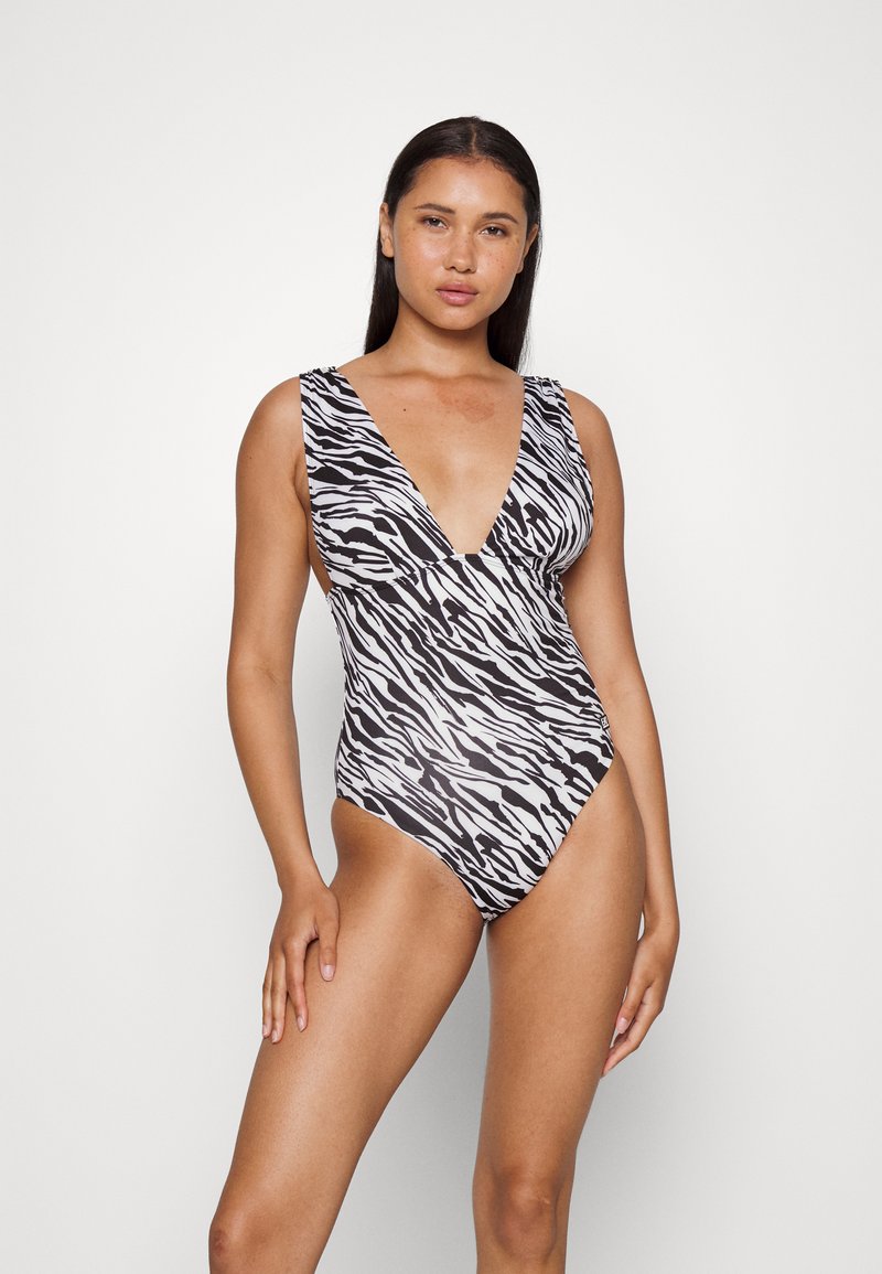 Costume da bagno intero con stampa zebra bianca e nera, con scollatura a V profonda, spalline larghe e aperture per le gambe ad alta scomparsa. Tessuto dalla superficie liscia.