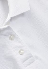 Polo shirt bianco con tessuto testurizzato, colletto e tre bottoni trasparenti. Il tessuto presenta un delicato motivo a coste.