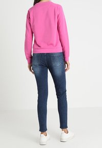 Sweat-shirt fuchsia à col rond, associé à un jean bleu foncé ajusté et des baskets blanches. Texture douce, design décontracté.