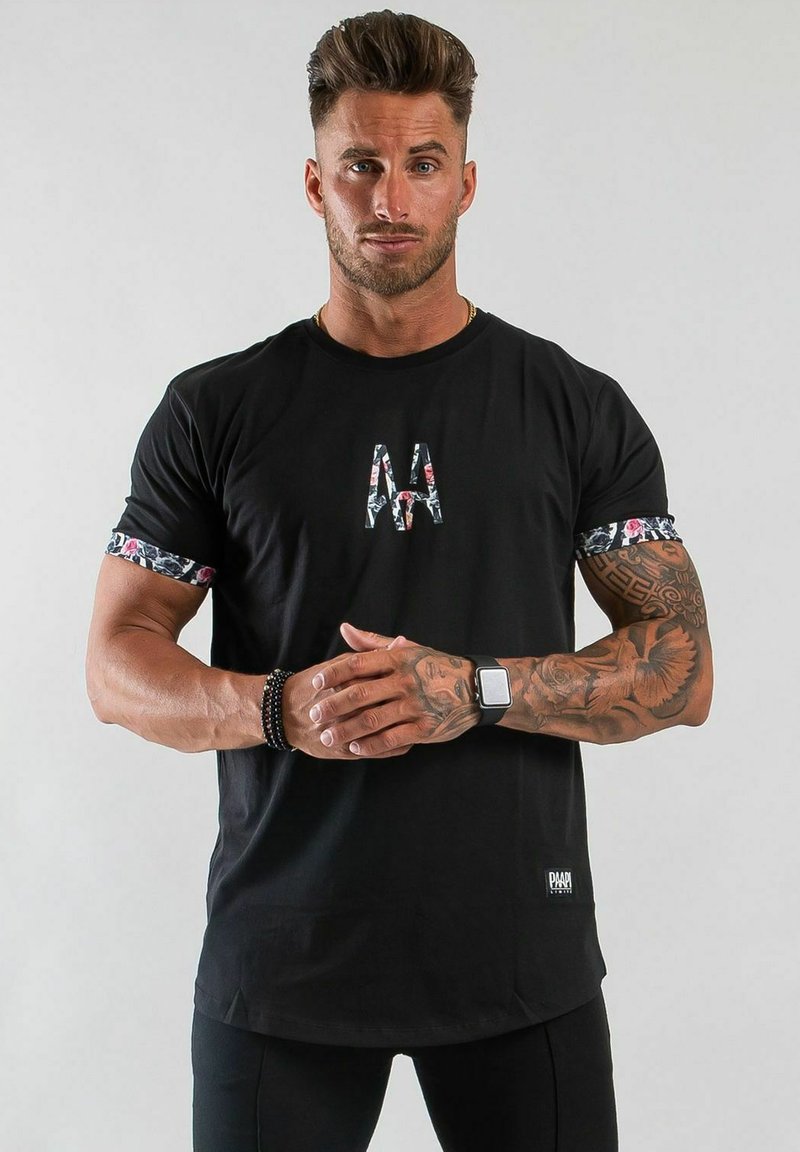 Svart t-shirt med blommigt mönster på ärmarna och en tryckt logotyp på framsidan. Har en avslappnad passform och är tillverkad av mjukt material.