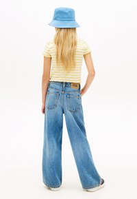 Ριγέ κίτρινη μπλούζα, ανοιχτόχρωμα γαλάζια τζιν παντελόνια με φαρδιά πόδια ψηλά στη μέση και πίσω τσέπες, και ένα μπλε καπέλο τύπου bucket. Απλός σχεδιασμός, casual εφαρμογή.