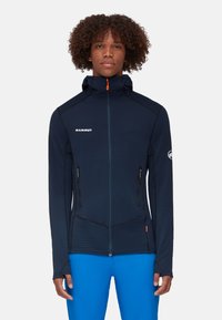 Marineblaues Mammut Zip-Up-Jacke mit Kapuze, ausgestattet mit schwarzen Akzenten, einem orangefarbenen Reißverschluss und strukturiertem Stoff. Enthält zwei Reißverschlusstaschen.