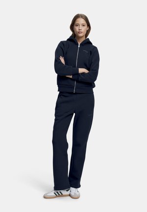 Marineblå hettegenser med glidelås og ribbestrikkede mansjetter, parret med matchende joggebukser; begge laget av myk stoff, med subtile merker.
