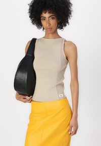 Beige geribbelde tanktop met een hoge halslijn, gecombineerd met een gele leren rok. Model draagt een zwarte, gebogen schoudertas.