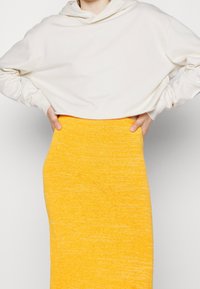 Hoodie cropped crema con cappuccio regolabile, abbinato a una gonna a maglia gialla con finitura testurizzata e vita aderente.