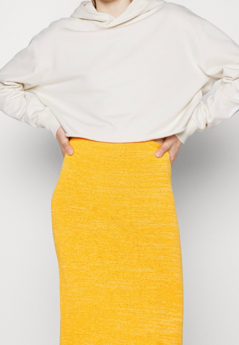 Hoodie cropped crema con cappuccio regolabile, abbinato a una gonna a maglia gialla con finitura testurizzata e vita aderente.