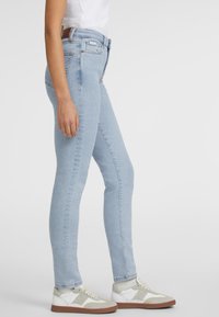 Ljusblå skinny jeans i denim, med hög midja, femfickorsdesign och subtila blekningar. Matchas med vita och grå sneakers.