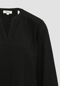 Zwarte blouse van lichtgewicht stof, met een V-hals, gathered schouders en een ontspannen pasvorm met subtiele textuurdetails.