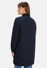 Cappotto lungo trapuntato di colore blu navy con colletto alto, caratterizzato da un motivo a diamante e polsini a costine, realizzato in un tessuto liscio e leggero.