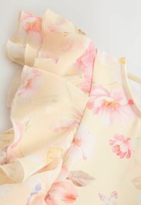 Virágos ruha világos sárga anyagból, rózsaszín és krémszínű virágokkal. A nyakkivágás fodros részletekkel díszített, amelyek textúrát és részletet adnak hozzá.