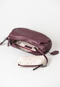 Bordeaux lederen tas met een gladde textuur, ritssluiting en interne rode accenten. Inclusief een kleinere tan etui met een subtiel patroon.