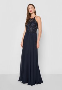 Tengerés kék ruha, amelynek testhezálló csipke felső része virágmintás hímzéssel és gyöngyökkel díszített, lebegő sifon szoknyával és vékony pántokkal rendelkezik.