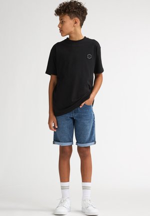 Zwart katoenen T-shirt met een klein logo, gecombineerd met opgerolde denim shorts en witte sneakers. Geaccentueerd met grijs gestreepte sokken.