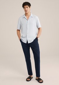 Lichtblauw kortmouwen overhemd met knopen, marineblauwe slim-fit broek en zwarte gestructureerde slip-op slippers. Soepele stof en eenvoudig ontwerp.