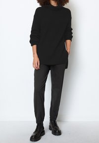 Maglione nero a costine con collo alto, abbinato a pantaloni neri a gamba affusolata e stivali neri chunk con lacci. La texture sembra morbida e accogliente.