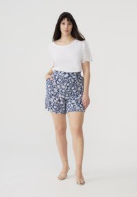 Top bianco a maniche corte con design a occhio sulle spalle, abbinato a pantaloni corti blu con stampa floreale, dotati di tasche laterali e vestibilità comoda.