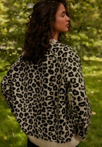 Pulover s uzorkom leoparda u krem i crnoj boji, s opuštenim krojem, rebrastim rubom i teksturiranom pletivom.