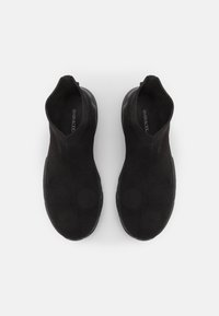 Chaussures noires à enfiler, fabriquées avec une tige en maille texturée, fermetures élastiquées au niveau des chevilles, et semelles en caoutchouc noires contrastantes.