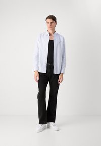 Camisa de botones a rayas azul claro, jeans negros y zapatillas blancas. La camisa tiene un cuello clásico y está hecha de tela tejida.