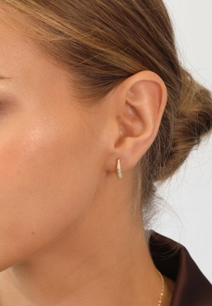 Gold hoop earring with a curved design. Features a line of small clear gemstones along the front edge. Lightweight and sleek appearance.