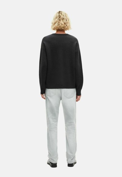 Maglione nero a vestibilità comoda con maniche larghe, abbinato a jeans grigi chiari e scarpe nere, visto da dietro.